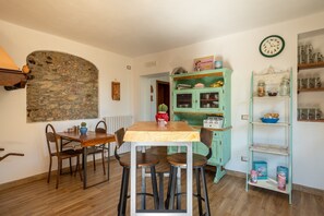 Un comedor con pared de piedra, una mesa de madera y sillas. Hay un armario verde con puertas de cristal y un reloj en la pared.