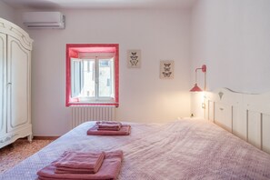 Un dormitorio con una cama, un radiador, un ventanal de marco rojo y decoración en la pared.