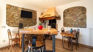 A dining area with stone walls, a fireplace, a television mounted on the wall, and a table with chairs.