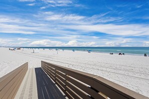 A beach with a wooden walkway leading to the shore, featuring a clear sky and calm sea.