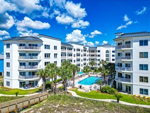 A multi-story hotel with a central pool surrounded by palm trees and a wooden deck.