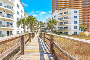A wooden boardwalk leading to a beachfront hotel with multiple balconies and palm trees. - Palm Beach B31 Gulf Front 3BR 2BA Corner Unit (Orange Beach)
