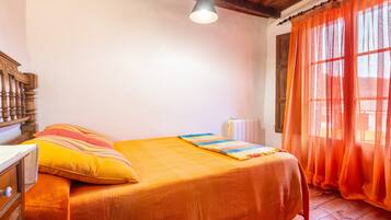 Un dormitorio con una cama, cabecero de madera, una ventana con cortinas naranjas y un radiador.