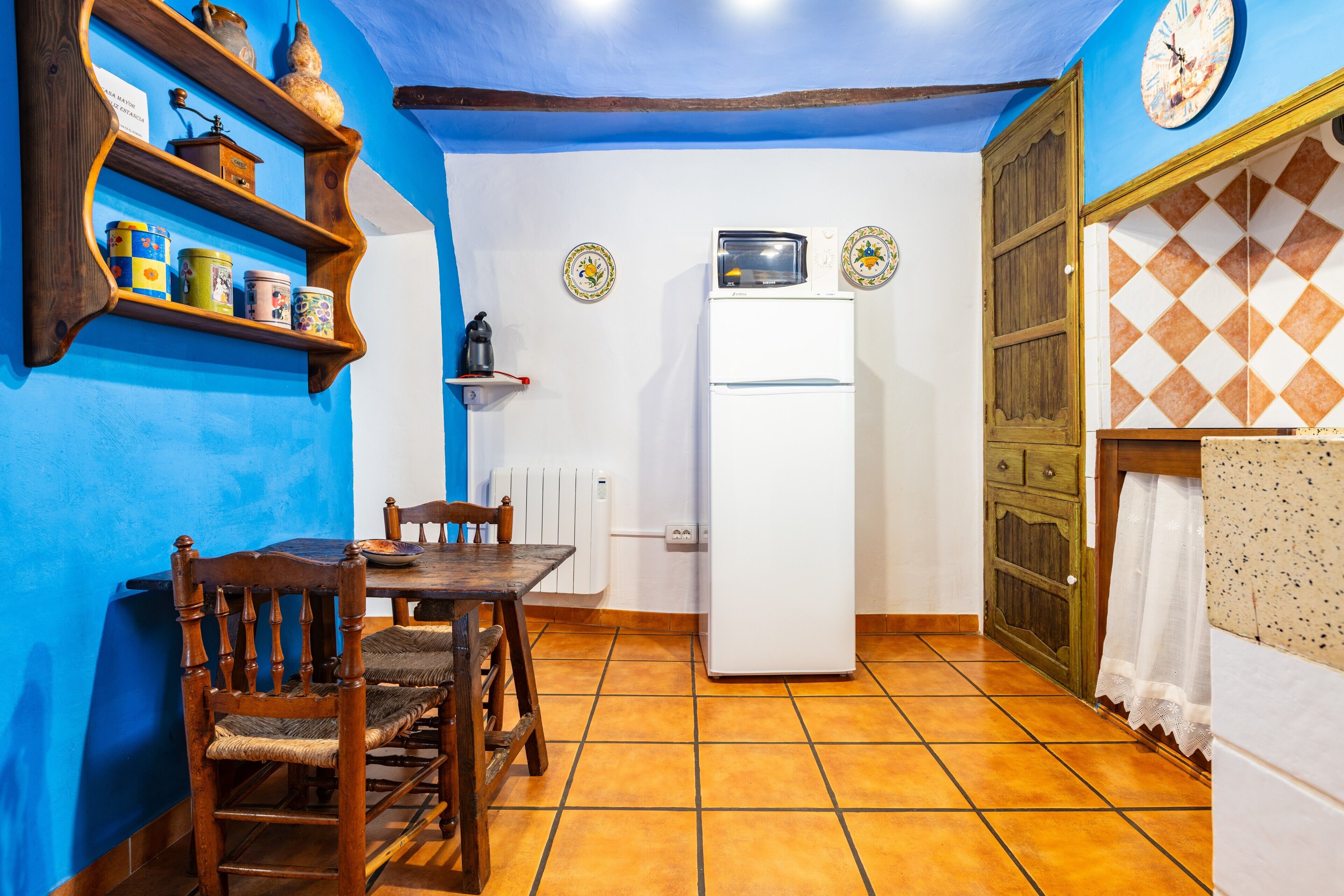 Una cocina con un refrigerador blanco, sillas de madera, una mesa y paredes azules.