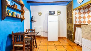 Una cocina con un refrigerador blanco, sillas de madera, una mesa y paredes azules.