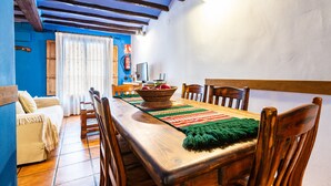 Un coin repas avec une table en bois, des chaises et un panier en osier rempli de fruits.