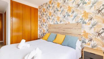 Habitación de hotel con un armario de madera, cama con ropa de cama blanca y pared con estampado de hojas tropicales.