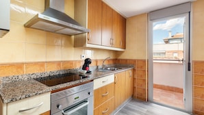 Una cocina con encimeras de granito, electrodomésticos de acero inoxidable, armarios de madera y un ventanal corredizo que da a un balcón.