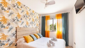 Habitación de hotel con cama, cabecera de madera, mesita de noche, televisor y cortinas.