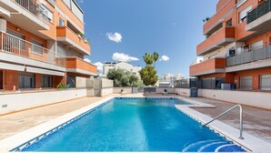Una piscina rectangular con agua azul cristalina, rodeada por una terraza con baldosas.