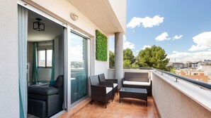 Un balcón con puerta de vidrio corrediza, muebles de mimbre y vista a la ciudad.