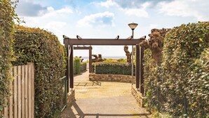 A pathway leading to a covered area with a pergola, surrounded by dense foliage and a stone wall. - Le Petit Voilier 'Family Spirit & Ocean' with Private Pool and Garden, PO30 (Pornic)