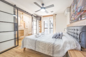 Un dormitorio con una cama, ventilador de techo, puerta corrediza de vidrio y un cuadro en la pared.