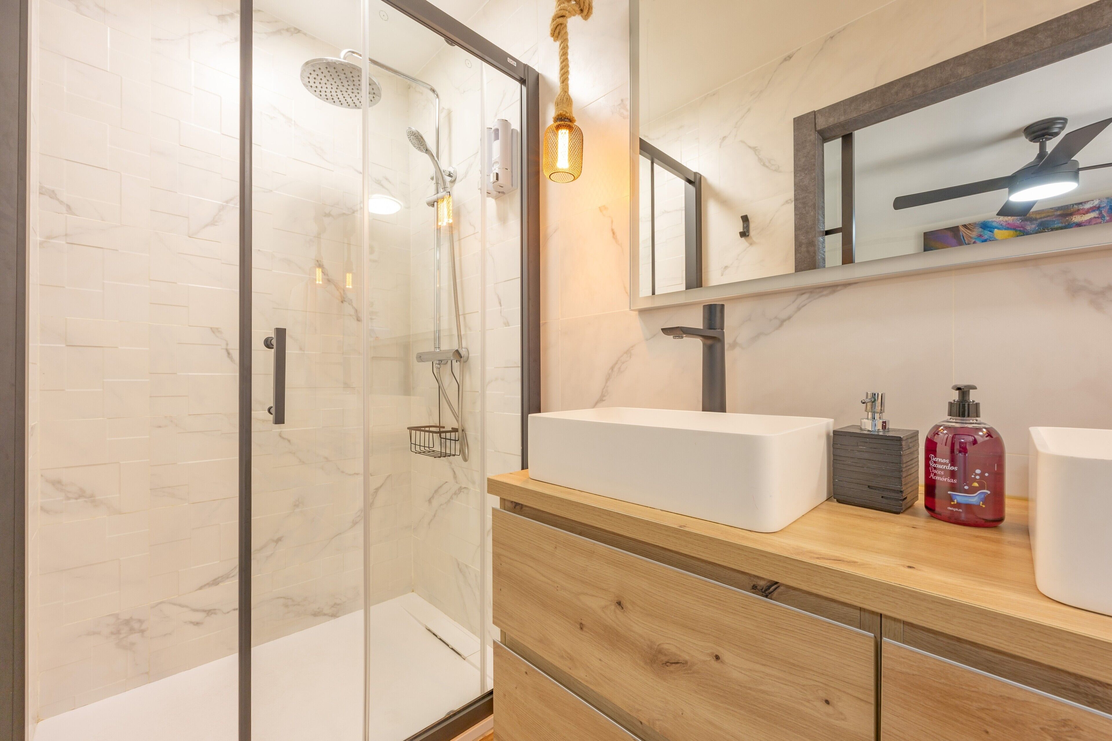 A modern bathroom with a glass shower enclosure, a wooden vanity with two sinks, and a mirror above the vanity.