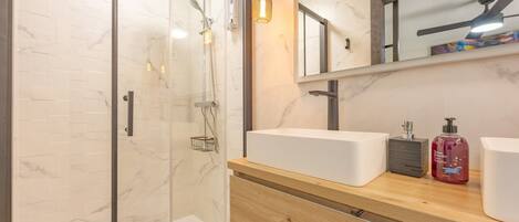 A modern bathroom with a glass shower enclosure, a wooden vanity with two sinks, and a mirror above the vanity.