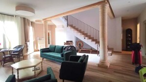 Un amplio salón con escaleras, un sofá verde, una mesa de centro y un comedor.