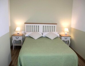Una cama con cabecera de madera, dos mesitas de noche con lámparas y una colcha verde.