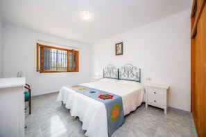 Ein Schlafzimmer mit einem Bett, einem Nachttisch, einem Fenster mit Holzrahmen und einem Bild an der Wand.