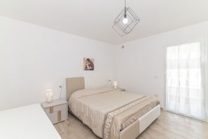 A bedroom with a bed, bedside tables, a wall-mounted light fixture, and a window with sheer curtains.