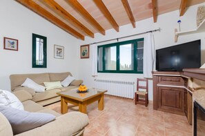 Una sala de estar con un sofá, una mesa de centro, un televisor y una ventana con cortinas.