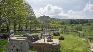 A rustic outdoor seating area with stone tables and benches, surrounded by trees and a view of a hill. - Discover Gîte Le Pradel in Les Estables
 (Les Estables)