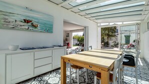 A modern kitchen with a dining area, a painting of boats, and a view through glass doors. - Holiday Home Le Havre du Capitaine with Private Terrace and Wi-Fi (19) (Pornic)