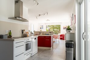 Une cuisine moderne avec des meubles blancs et rouges, des appareils en acier inoxydable et un coin repas agrémenté d’une chaise rouge.