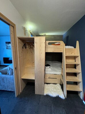 Una cama individual superpuesta con escalera de madera, un estante pequeño y una barra para colgar.
