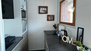 A compact kitchen with a microwave, oven, and coffee maker. There are two framed pictures on the wall and a window with a view.