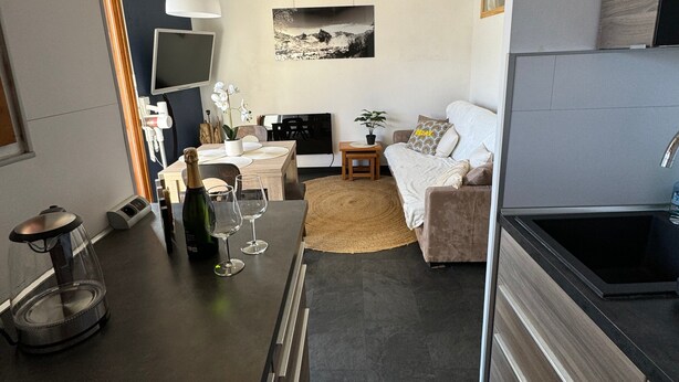 A modern kitchen with a dining area, a flat-screen TV, and a bed with a view.