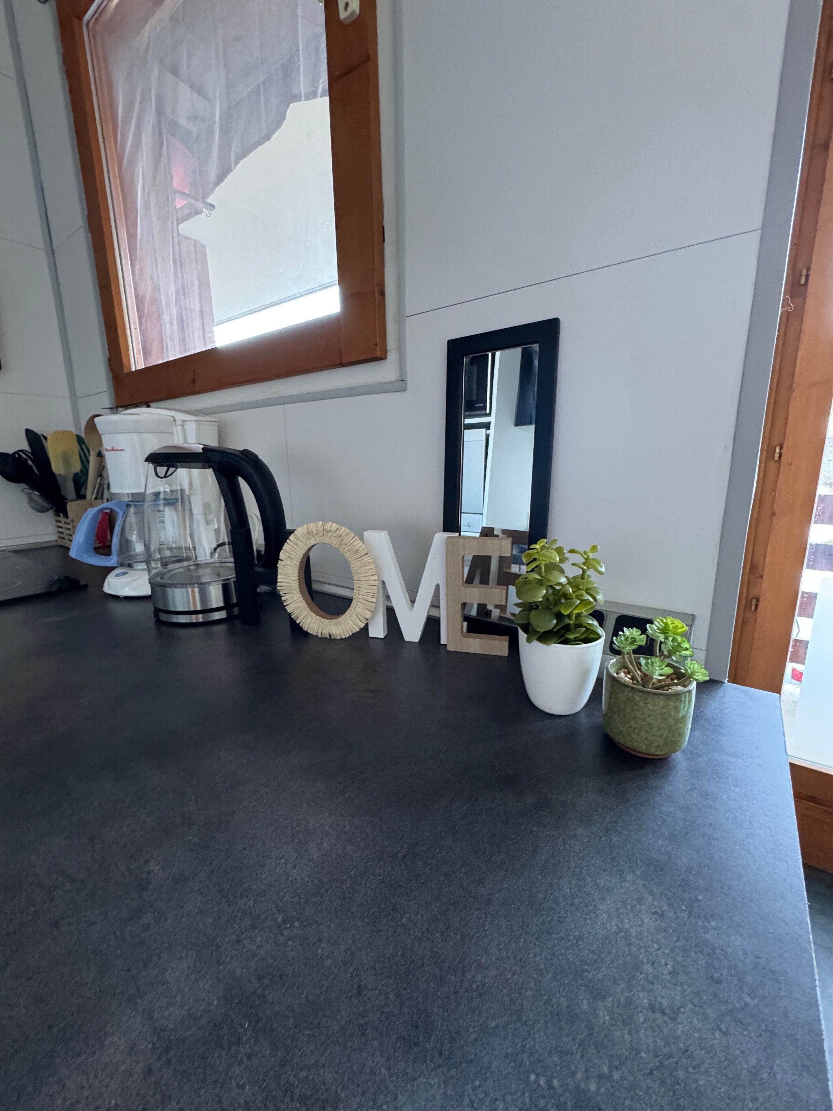 A kitchen counter with a coffee maker, a kettle, a potted plant, and decorative letters spelling 'HOME'.