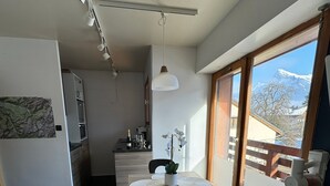 A modern kitchen with a dining area, a view of mountains, and a balcony.