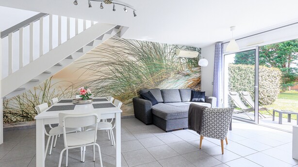 Een modern interieur met een trap, een eethoek, een bank en een uitzicht door grote glazen deuren.