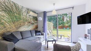 Een moderne woonkamer met een grijze bank, een salontafel en een aan de muur bevestigde televisie.