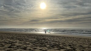 Een strand met voetafdrukken die naar het water leiden, een heldere lucht en de zon die ondergaat of opkomt.