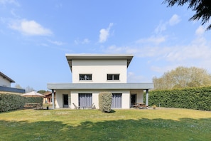 A modern two-story house with a flat roof, a covered patio, and a well-maintained lawn.