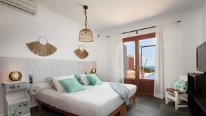 A bedroom with a bed, bedside tables, a TV, and a view of the sea. - Country House 'Ses Penyes' with Sea View, Wi-Fi and Air Conditioning (Santanyí)