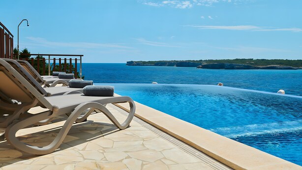 A poolside area with lounge chairs, a clear view of the sea, and a stone-tiled floor. - Country House 'Ses Penyes' with Sea View, Wi-Fi and Air Conditioning (Santanyí)
