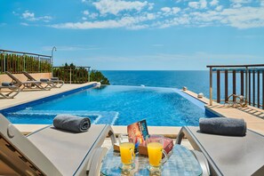 Blick auf das Schwimmbecken mit Liegestühlen, einem Glastisch mit Getränken und den Blick aufs Meer.
