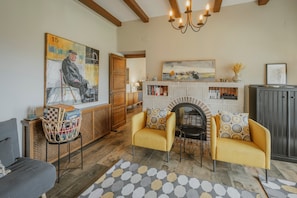 Una sala de estar con chimenea, dos sillones amarillos, un tapete estampado y un cuadro en la pared.