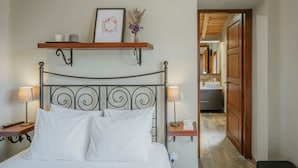 Un dormitorio ordenado con cama, mesitas de noche, una estantería con un cuadro enmarcado y un baño visible a través de una puerta abierta.