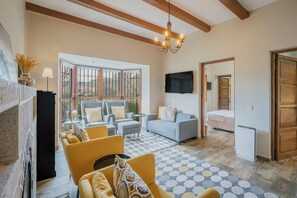 A living room with a fireplace, sofa, armchair, and a TV mounted on the wall. - Chalet 'Finca El Aguilojo' with Private Pool, Private Terrace and Wi-Fi (Mombeltrán)