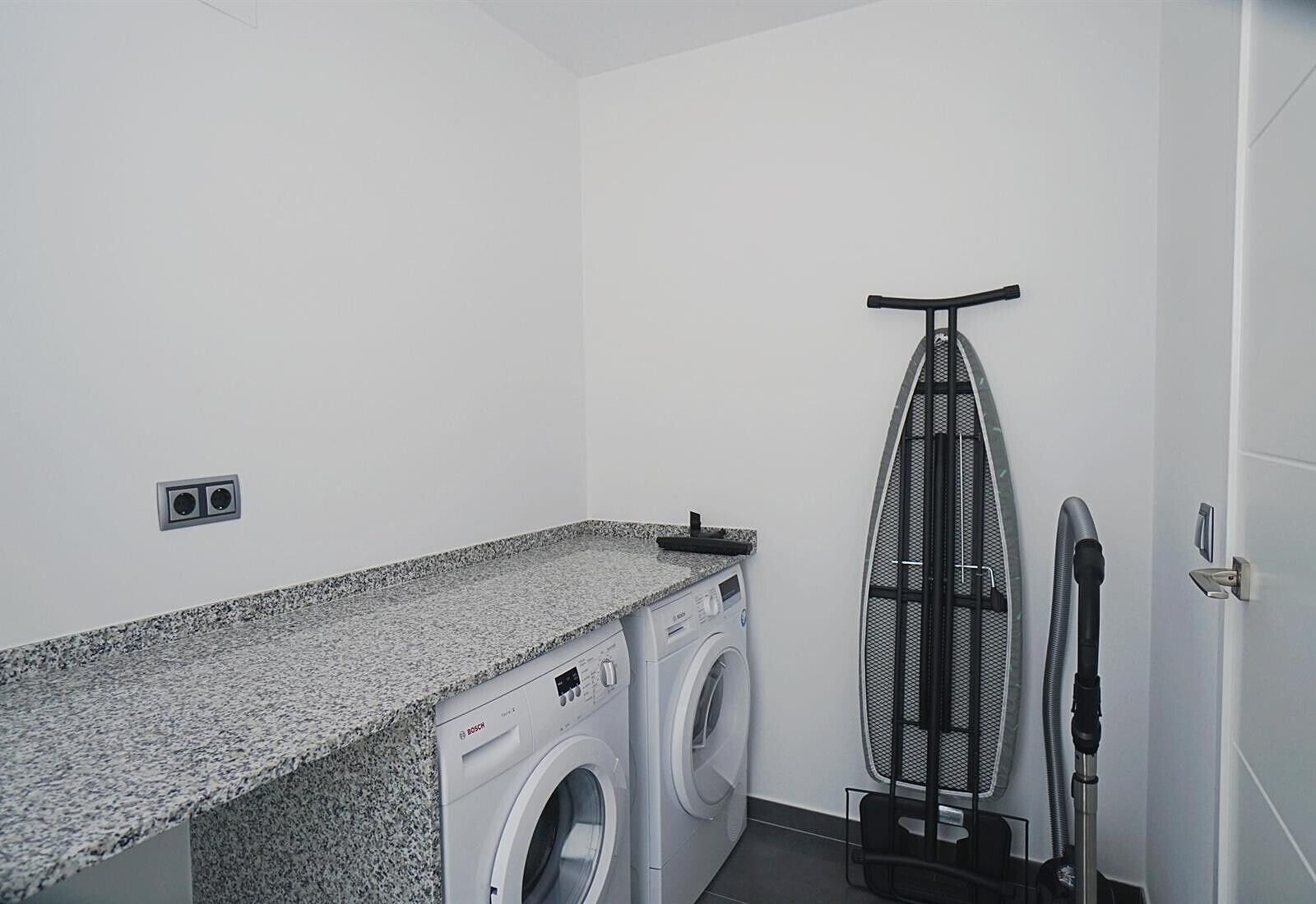 A laundry room with a washing machine, dryer, iron, and ironing board.