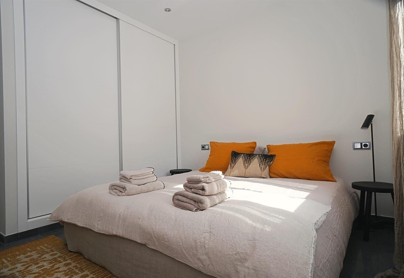 Een hotelkamer met een bed, twee kussens, een nachtkastje, een lamp en een kledingkast.