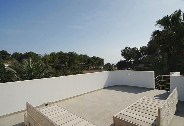 A rooftop terrace with a curved white wall, a wooden bench, and a metal railing.