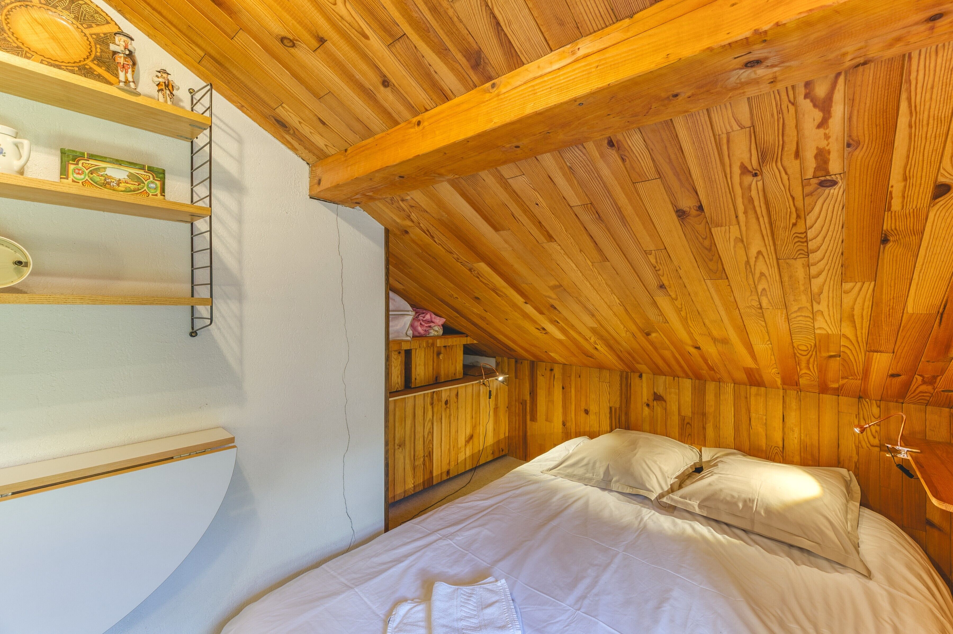 Een kamer met houten lambrisering, een bed, planken en een trap.