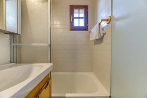 A bathroom with a bathtub, a shower, a window, and a towel rack.