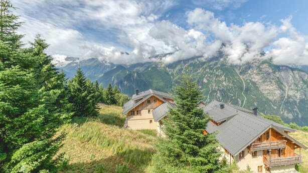 Un chalet doté d’un balcon, entouré d’arbres et de montagnes.