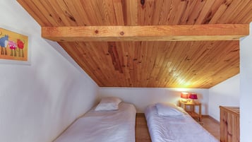Et lille, hyggeligt værelse med to senge, træloft, et billede på væggen og et sengebord med en lampe.