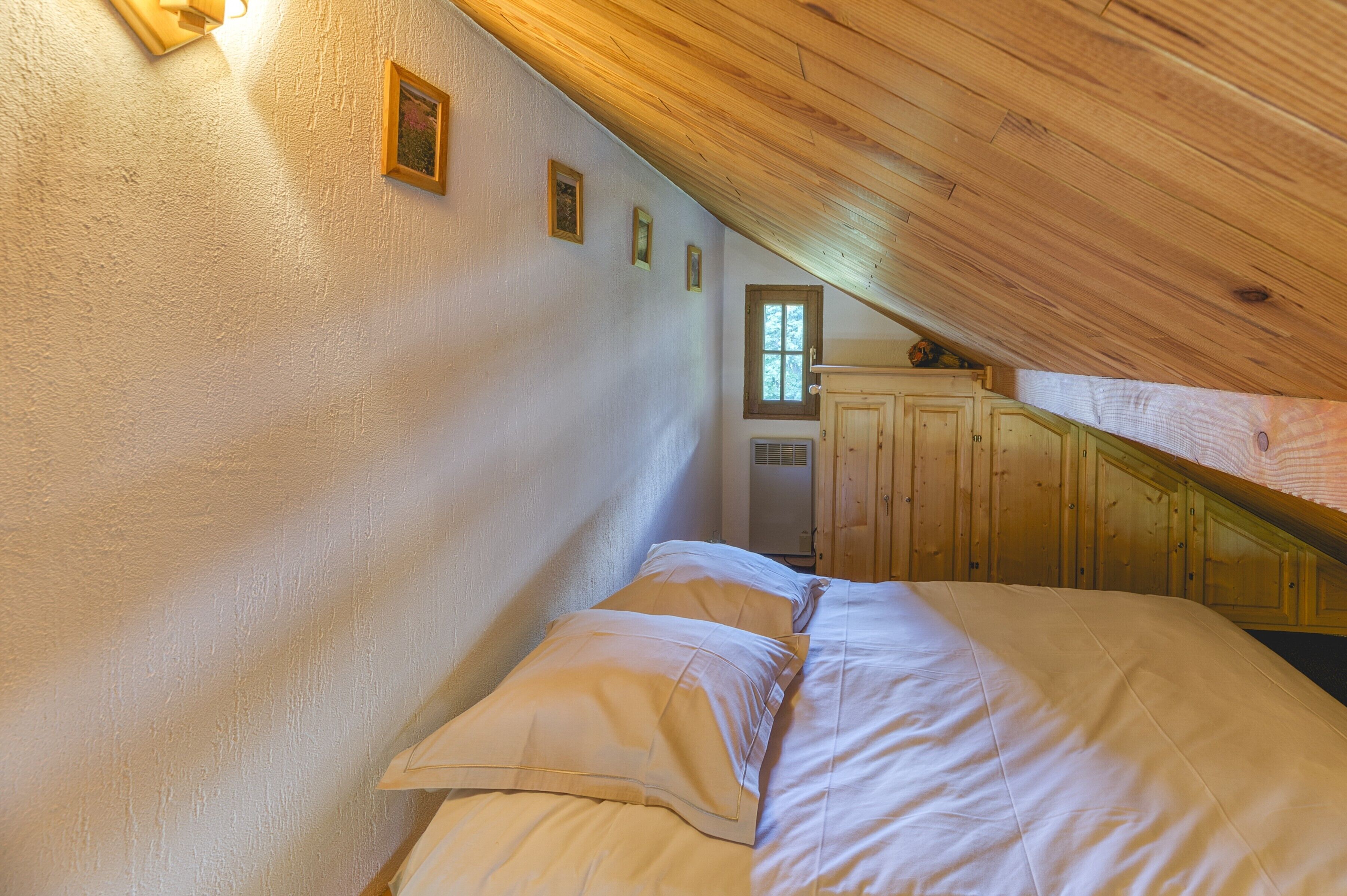 Ein Schlafzimmer mit Holzboden, einem Bett mit weißer Bettwäsche, einem Fenster und Holzschränken.